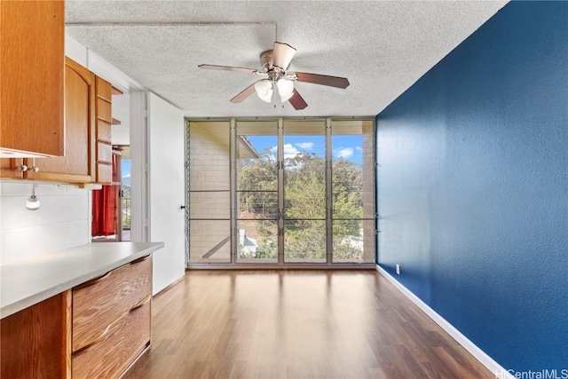 unfurnished dining area with expansive windows, a textured ceiling, baseboards, and wood finished floors