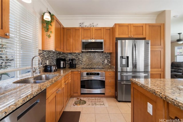 kitchen featuring brown cabinetry, ornamental molding, a sink, stainless steel appliances, and backsplash