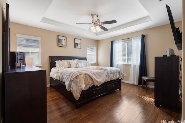 bedroom featuring dark wood-style floors, baseboards, a tray ceiling, and ceiling fan