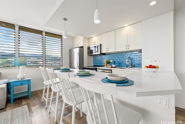 kitchen featuring decorative backsplash, appliances with stainless steel finishes, a sink, wood finished floors, and a kitchen breakfast bar