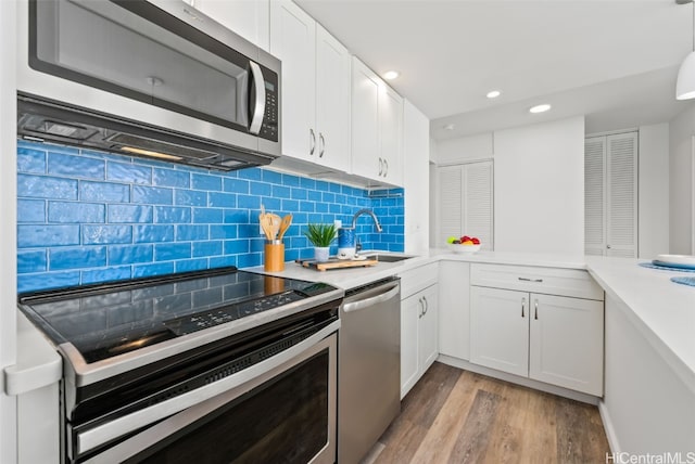 kitchen with stainless steel appliances, a sink, white cabinetry, light countertops, and light wood-type flooring