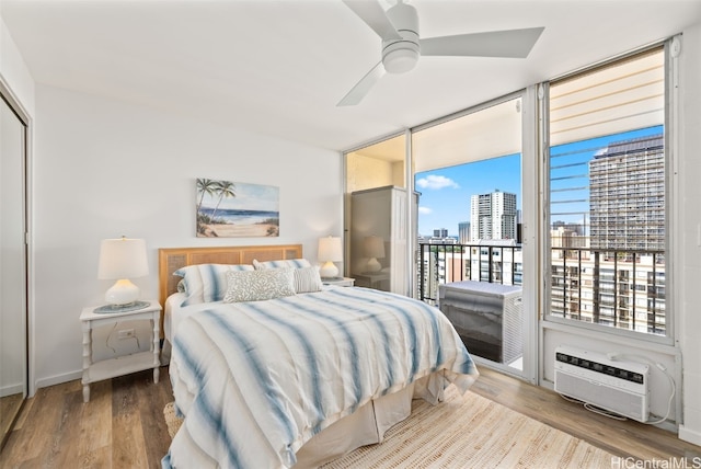 bedroom featuring wood finished floors, access to outside, a wall mounted AC, a view of city, and a wall of windows