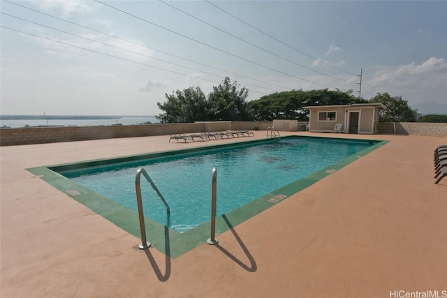 pool with a water view, fence, an outdoor structure, and a patio