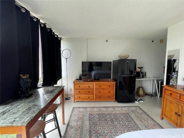 bedroom featuring finished concrete flooring, a textured ceiling, and freestanding refrigerator