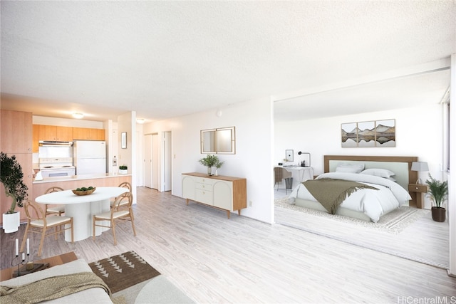 bedroom featuring light hardwood / wood-style flooring, a textured ceiling, and white fridge