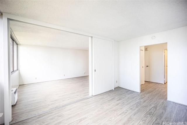 unfurnished room featuring a wall mounted AC, a textured ceiling, and light wood-type flooring