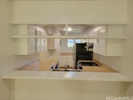 kitchen with sink, white cabinetry, stainless steel fridge, kitchen peninsula, and stove