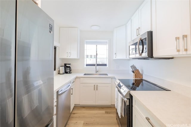 kitchen featuring appliances with stainless steel finishes, sink, white cabinets, and light wood-type flooring