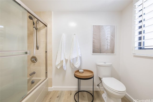 bathroom featuring wood-type flooring, combined bath / shower with glass door, and toilet