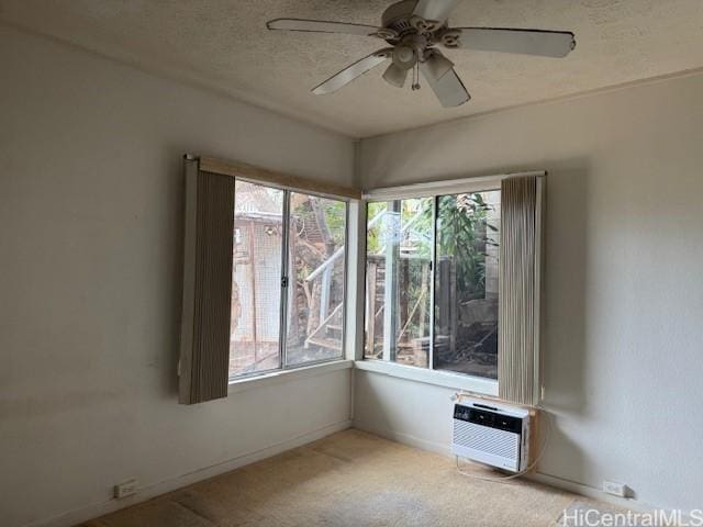 empty room featuring light carpet, baseboards, a ceiling fan, a wall unit AC, and a textured ceiling