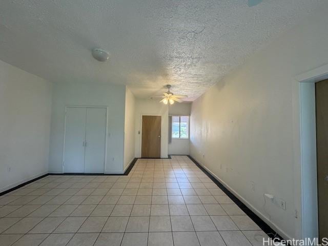 empty room with a ceiling fan, light tile patterned flooring, and baseboards