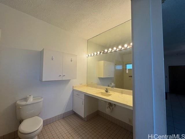 bathroom with toilet, a sink, a textured ceiling, tile patterned flooring, and baseboards