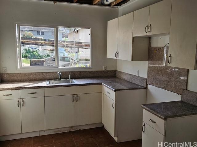 kitchen featuring dark countertops, white cabinets, a sink, and dark tile patterned flooring