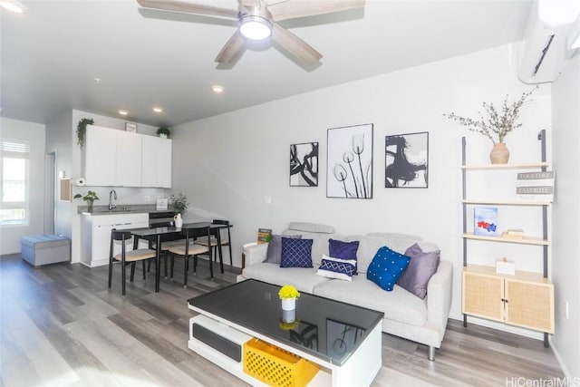 living room featuring sink, wood-type flooring, an AC wall unit, and ceiling fan