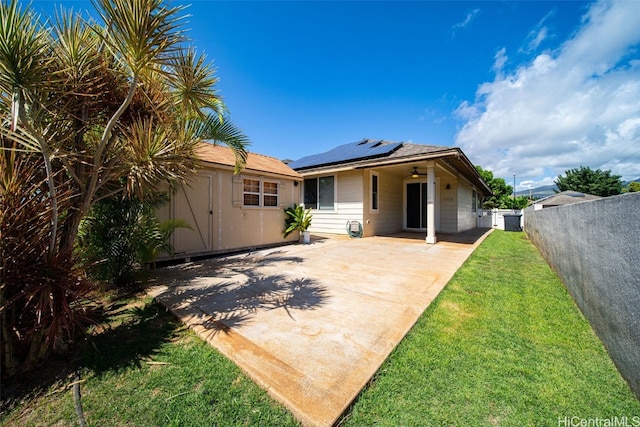 rear view of property with an outbuilding, a yard, solar panels, a ceiling fan, and fence