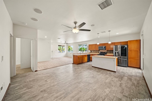 kitchen with visible vents, brown cabinetry, appliances with stainless steel finishes, open floor plan, and a center island