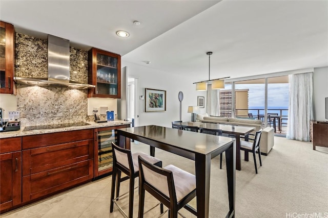 kitchen with pendant lighting, wall chimney range hood, floor to ceiling windows, black electric stovetop, and decorative backsplash