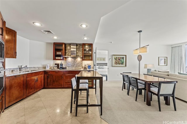 kitchen featuring decorative light fixtures, sink, light colored carpet, light stone counters, and wall chimney range hood