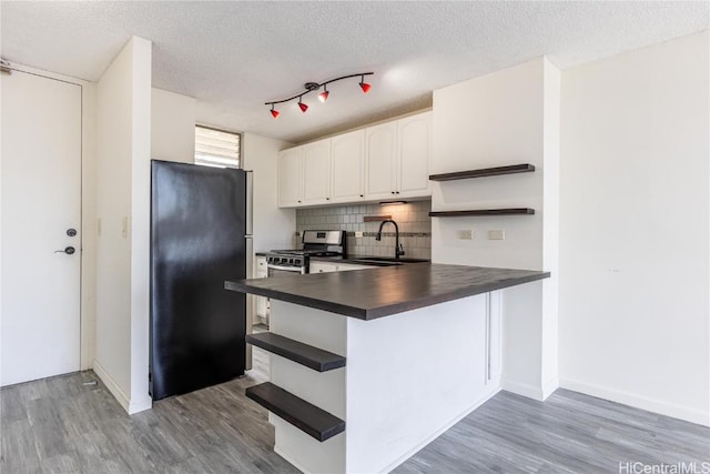 kitchen with sink, hardwood / wood-style flooring, white cabinetry, backsplash, and black fridge