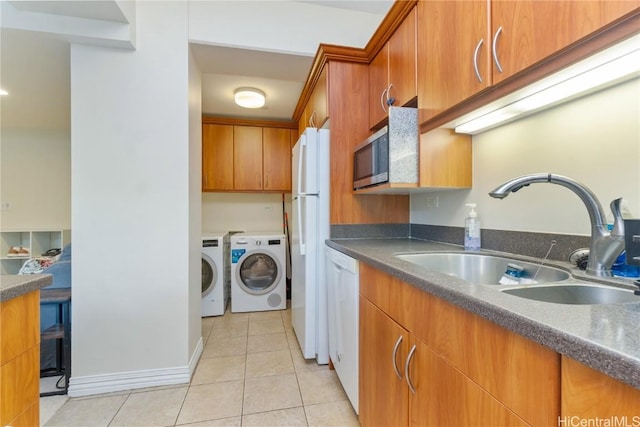 kitchen with washing machine and clothes dryer, light tile patterned floors, dark countertops, a sink, and white appliances