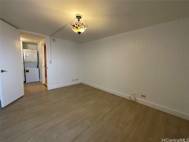 empty room with hardwood / wood-style floors and stacked washer / dryer