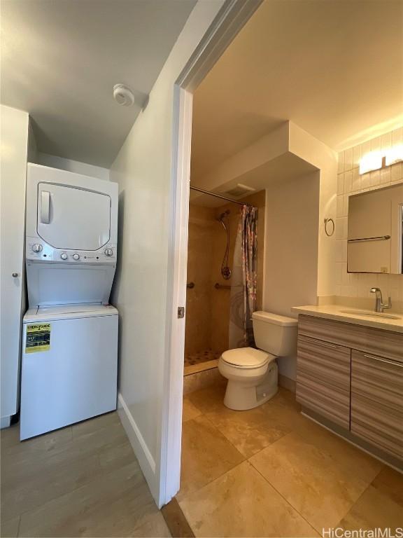 bathroom with vanity, stacked washer and dryer, curtained shower, and toilet