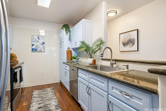 kitchen with dark wood-type flooring, a sink, white cabinetry, appliances with stainless steel finishes, and dark stone countertops