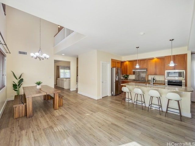 kitchen featuring pendant lighting, light stone countertops, stainless steel appliances, and light wood-type flooring