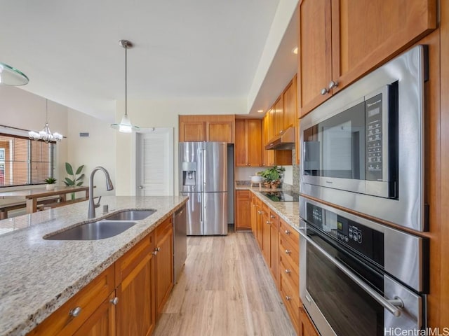 kitchen featuring sink, stainless steel appliances, light stone counters, decorative light fixtures, and exhaust hood