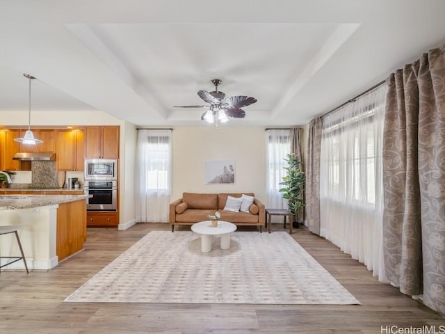 living room featuring ceiling fan, a tray ceiling, and light wood-type flooring