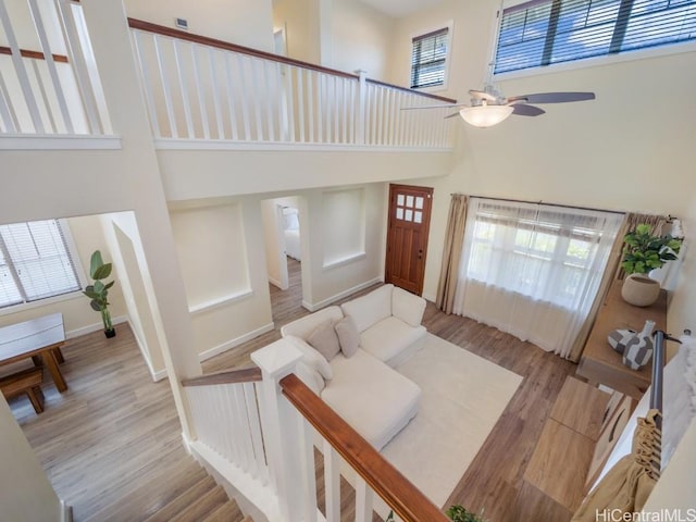 living room with ceiling fan, a towering ceiling, and light wood-type flooring