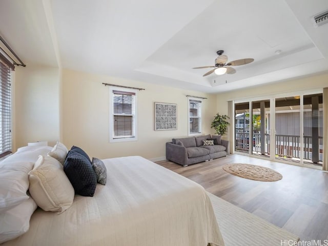 bedroom with a raised ceiling, access to exterior, ceiling fan, and light hardwood / wood-style flooring