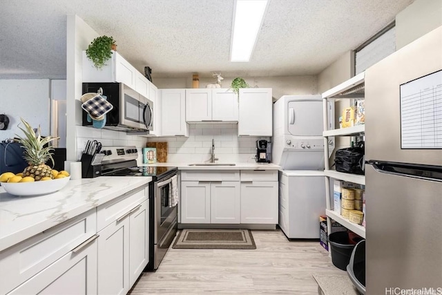 kitchen featuring stainless steel appliances, sink, stacked washer / drying machine, and white cabinets