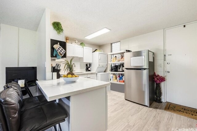 kitchen with stacked washer and dryer, stainless steel refrigerator, white cabinetry, a kitchen bar, and kitchen peninsula