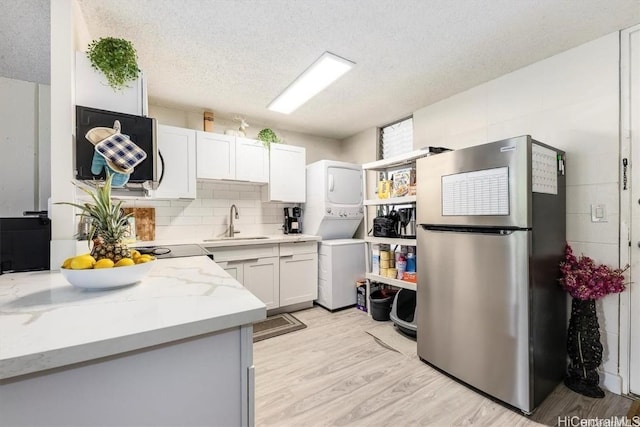 kitchen featuring sink, a textured ceiling, light wood-type flooring, stainless steel fridge, and white cabinets