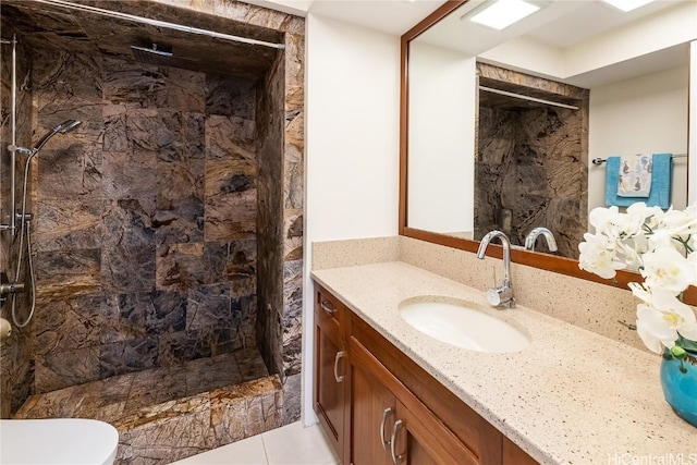 full bathroom with toilet, tiled shower, and vanity