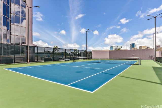 view of tennis court with a view of city and fence