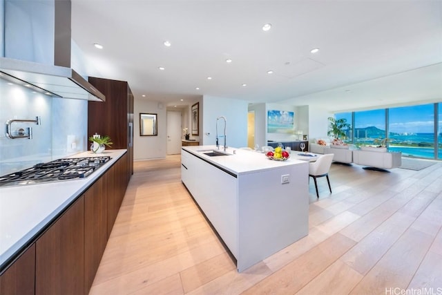 kitchen with an island with sink, modern cabinets, island exhaust hood, light countertops, and a sink