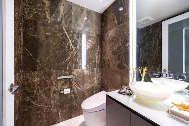 bathroom featuring toilet, vanity, visible vents, and tile walls