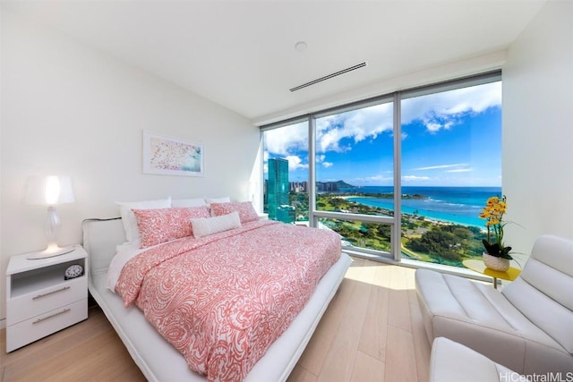 bedroom featuring light wood-style floors, a water view, and floor to ceiling windows