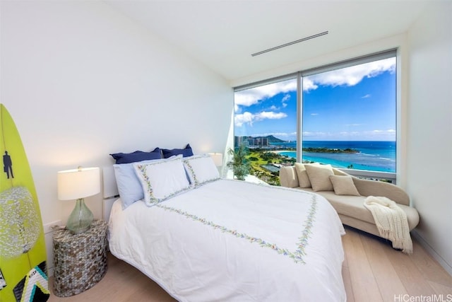 bedroom featuring a wall of windows, a water view, and light wood-style floors