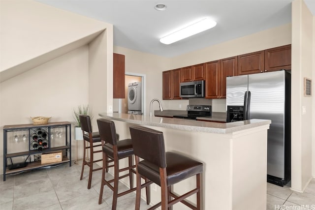 kitchen with light tile patterned floors, washer / clothes dryer, a kitchen bar, and stainless steel appliances