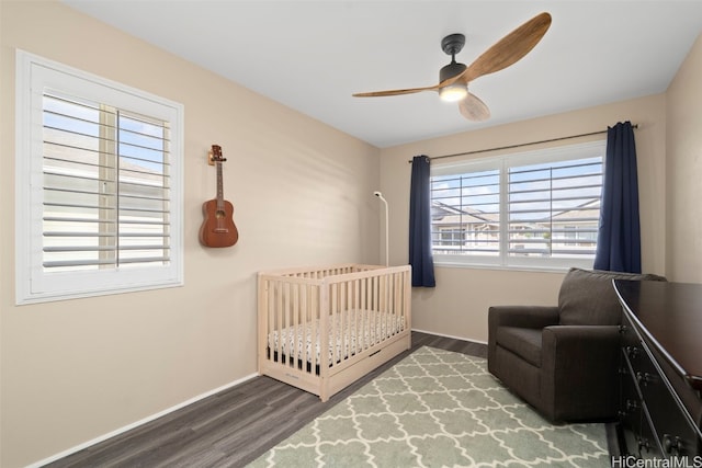 bedroom featuring baseboards, a nursery area, wood finished floors, and a ceiling fan