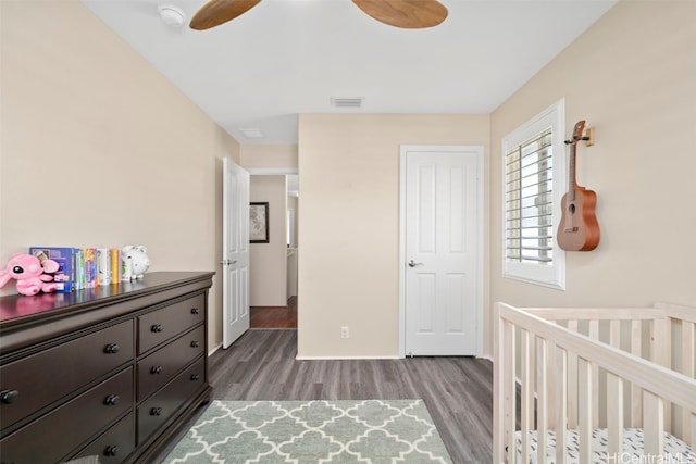 bedroom featuring wood finished floors, visible vents, baseboards, ceiling fan, and a nursery area