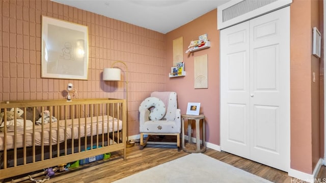 bedroom with a nursery area, dark hardwood / wood-style flooring, and a closet