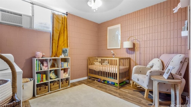 bedroom featuring hardwood / wood-style flooring, a crib, ceiling fan, and tile walls