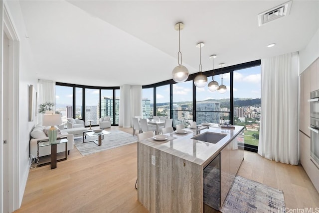 kitchen featuring sink, floor to ceiling windows, decorative light fixtures, and an island with sink