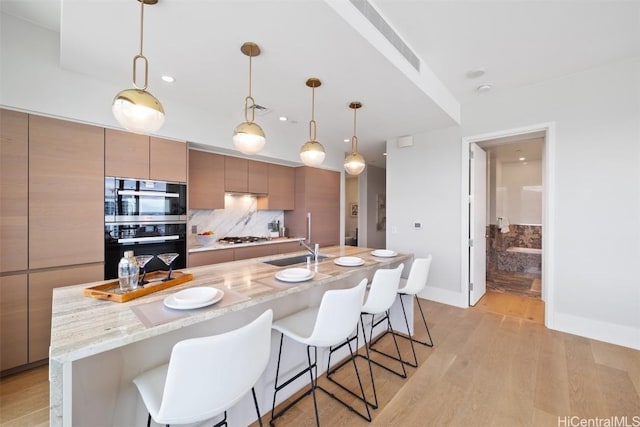 kitchen with pendant lighting, sink, light hardwood / wood-style flooring, light stone countertops, and stainless steel gas cooktop