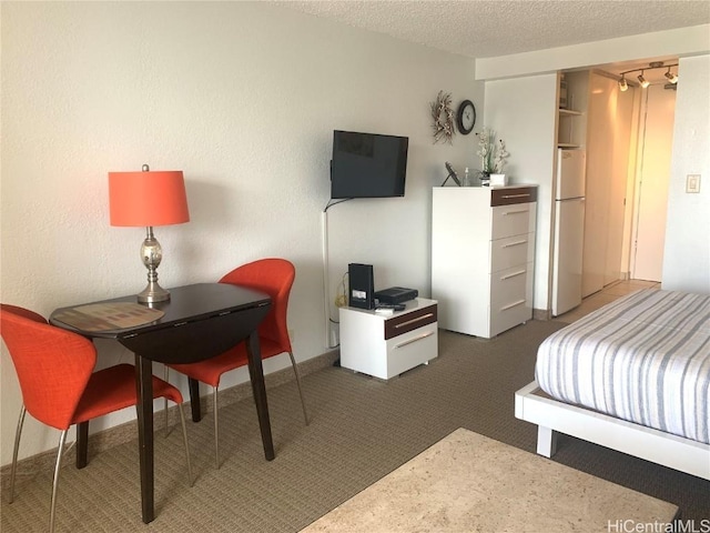 bedroom with dark colored carpet, white fridge, and a textured ceiling