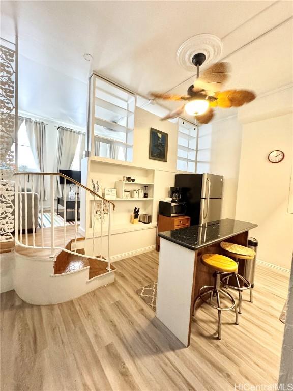 kitchen featuring ceiling fan, stainless steel fridge, a breakfast bar, and light hardwood / wood-style flooring